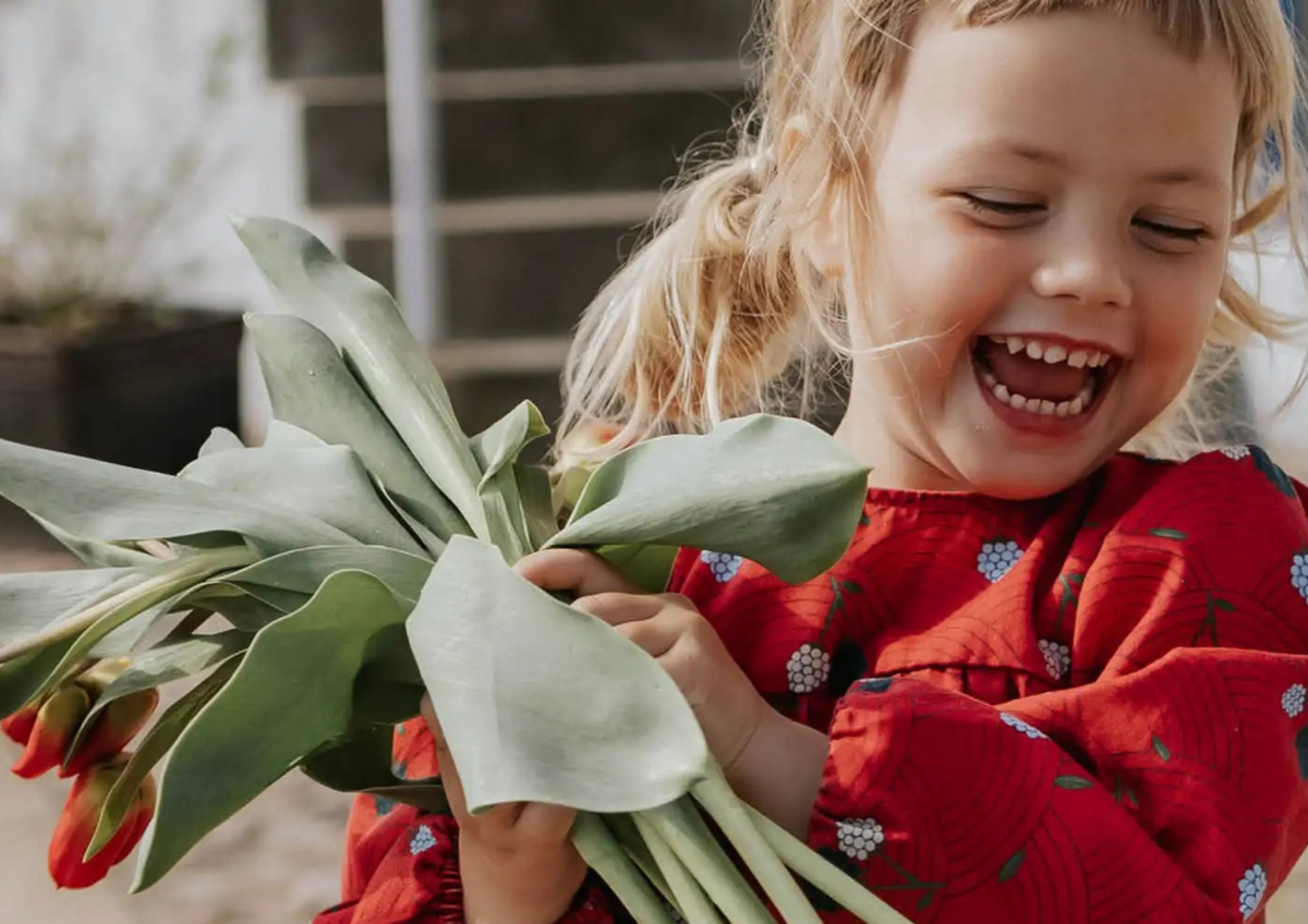 Smiling young girl in a red floral dress holding a large bouquet of red tulips.