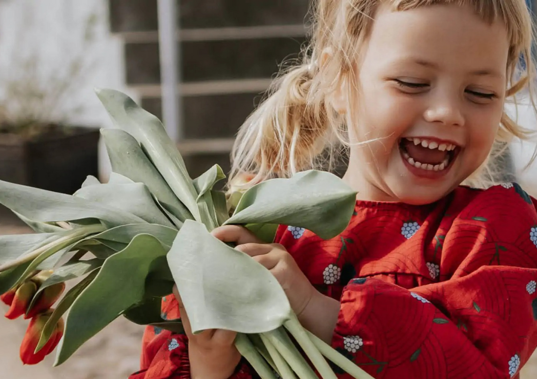 Smiling young girl in a red floral dress holding a large bouquet of red tulips.