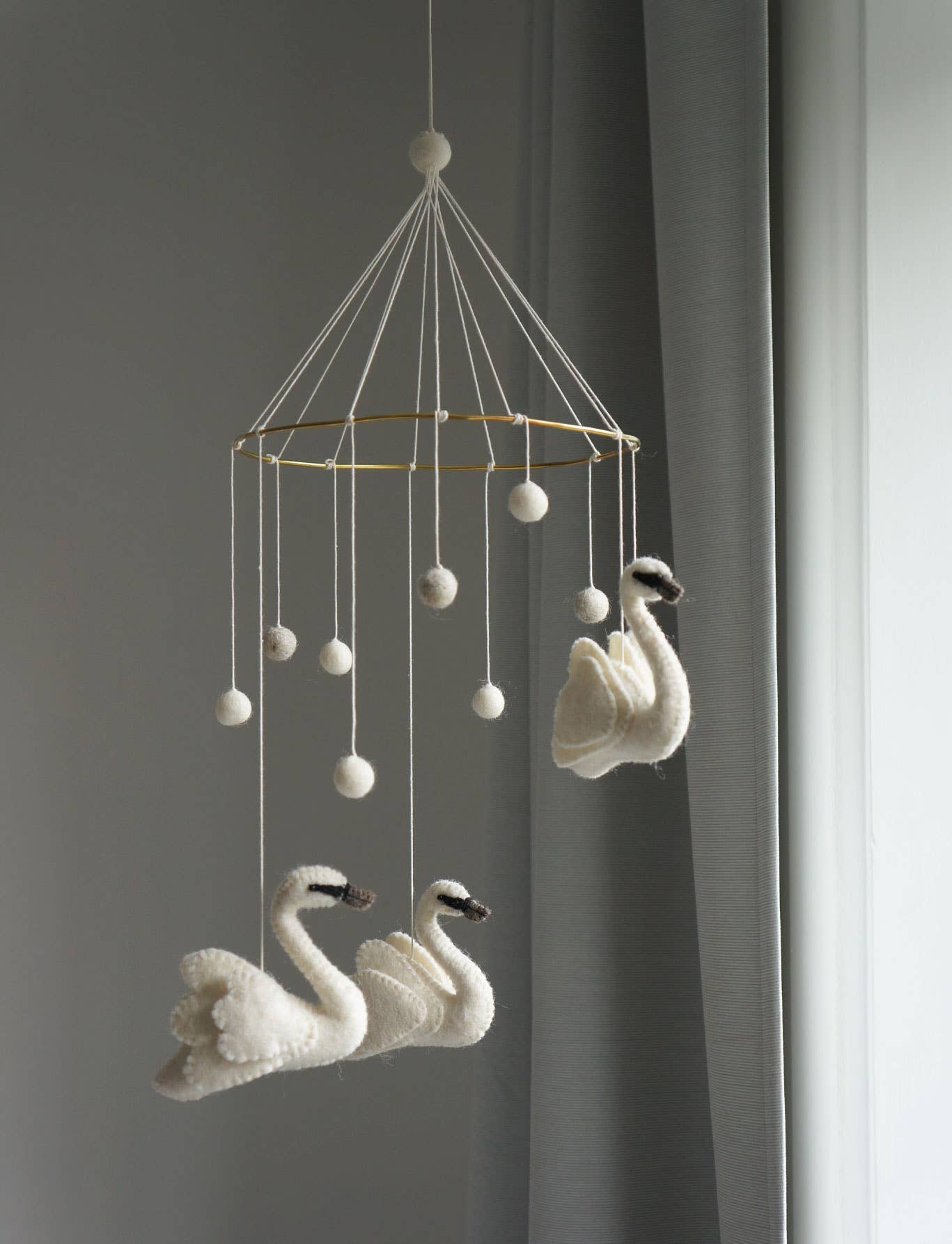 Decorative mobile with swan shapes hanging against a gray wall.