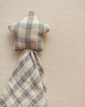 A star-shaped baby lovey blanket with a soft plaid pattern in beige and gray, shown on a neutral beige fabric background.