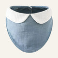 A crinkled cotton muslin baby bib in dusty blue with a contrasting white Peter Pan collar, shown on a plain white background.