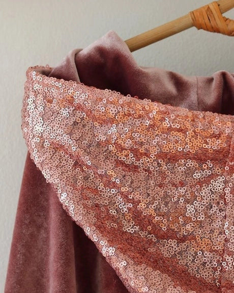 Pink fabric with sequin trim on a wooden hanger against a neutral background