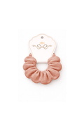 A dusty rose pink fabric scrunchie attached to a white paper display card with gold foil detailing, set against a plain white background.
