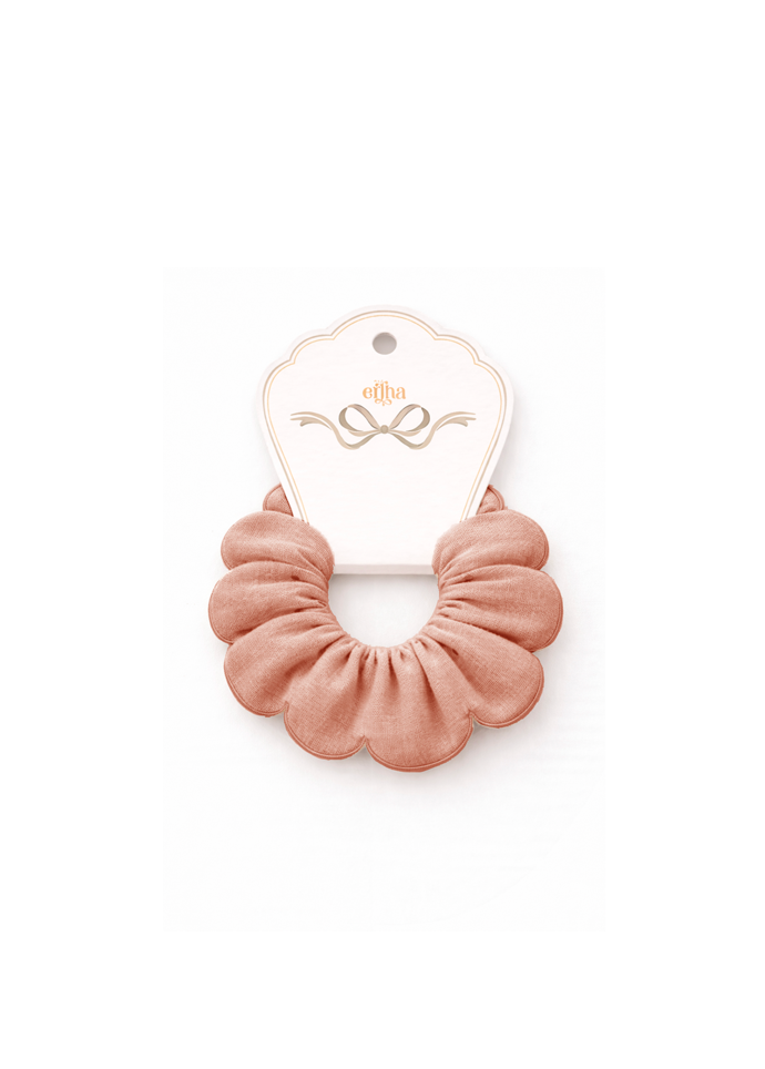 A dusty rose pink fabric scrunchie attached to a white paper display card with gold foil detailing, set against a plain white background.