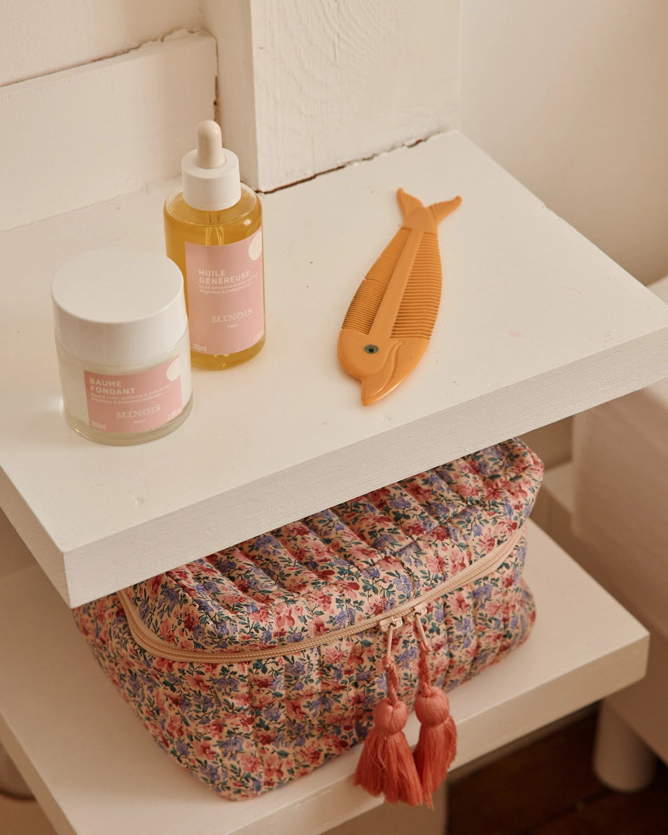 Floral bag, bottle, and container on a white shelf in a bathroom setting