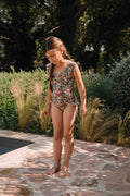 Young girl in a floral swimsuit standing on a stone path with greenery in the background