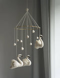 Decorative mobile with swan shapes hanging against a gray wall.