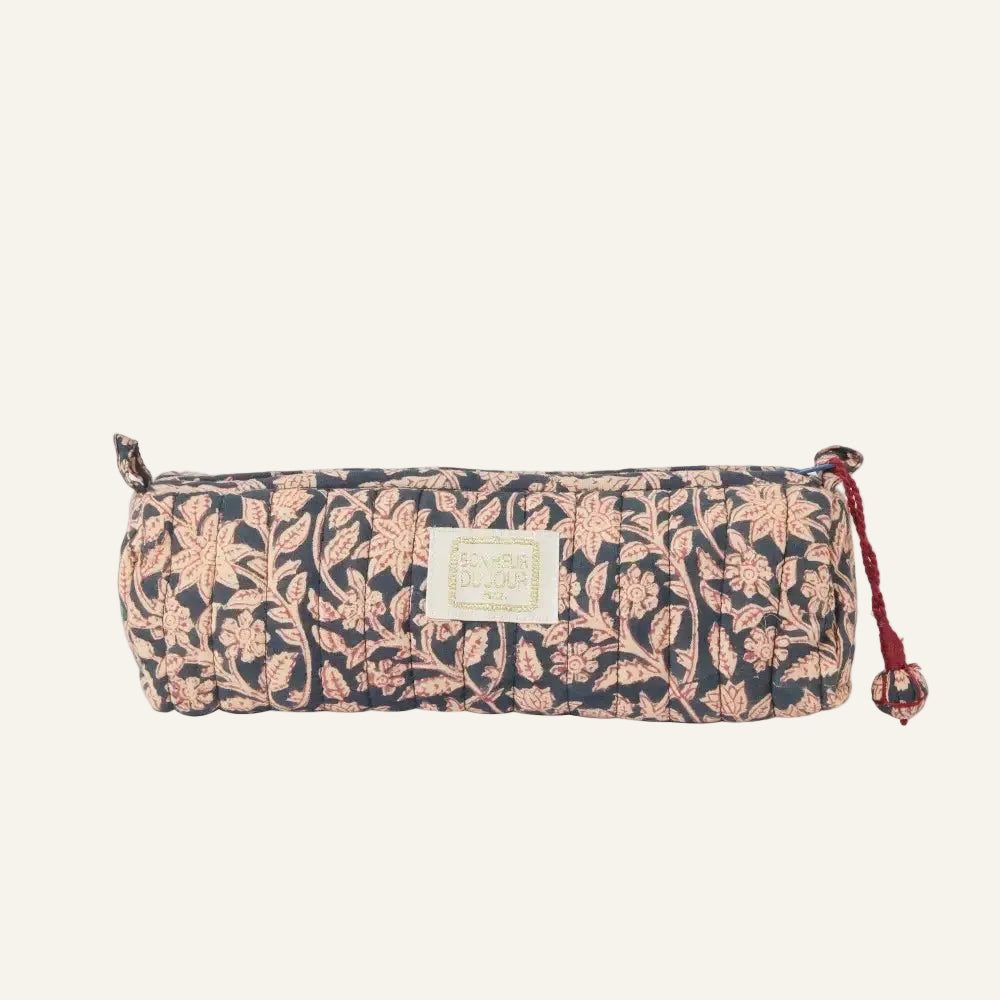 A rectangular fabric pencil case with a navy blue background and a pink floral block print pattern, featuring a cream-colored brand label on the front and a red tassel zipper pull.