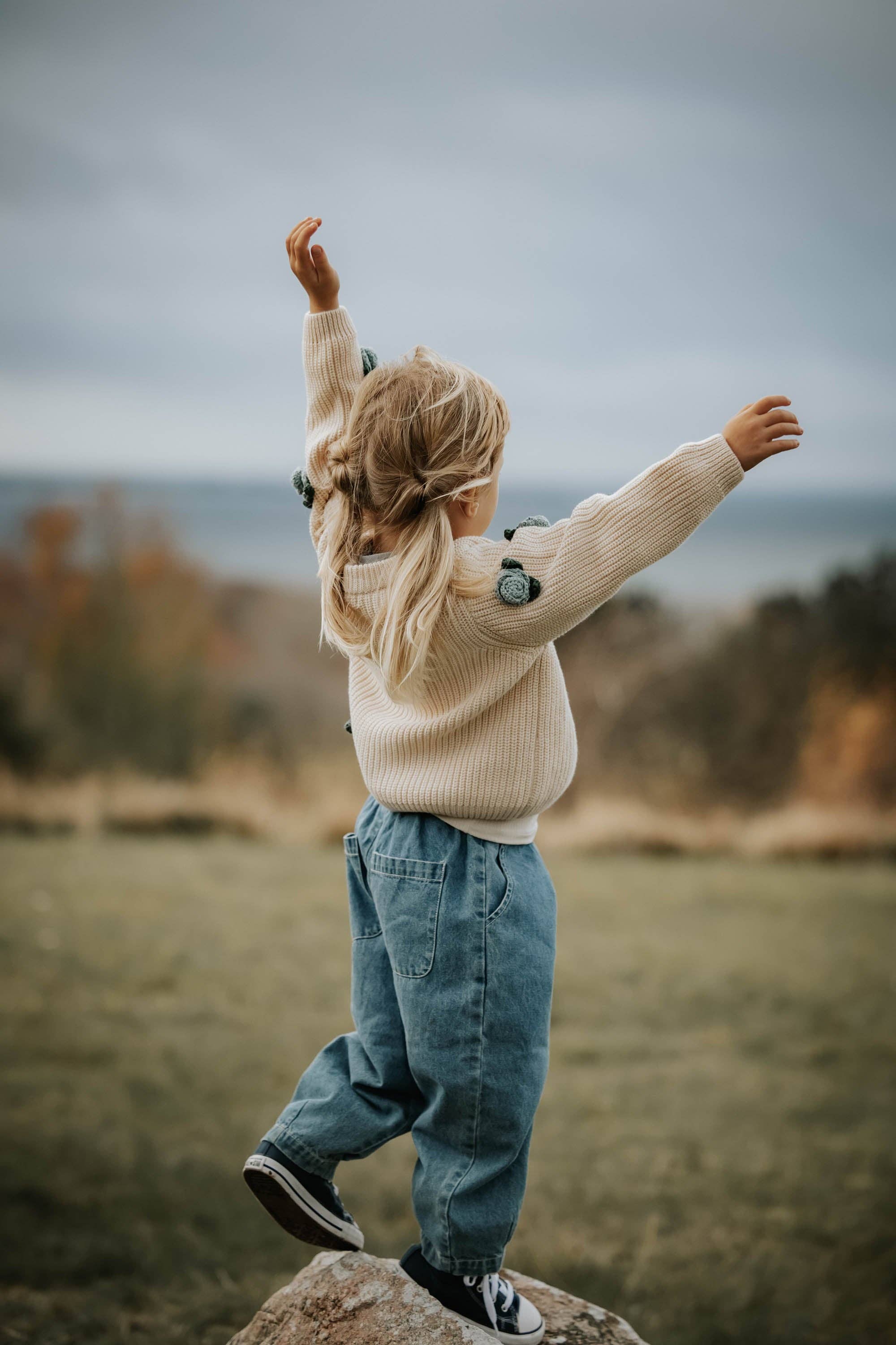 Person standing on a rock with arms outstretched in a natural setting