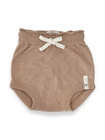 A pair of baby bloomers in a warm taupe-beige color, featuring a textured knit pattern, a scalloped waistband, and a small white bow tied at the front. A small fabric brand tag is visible on the right leg.