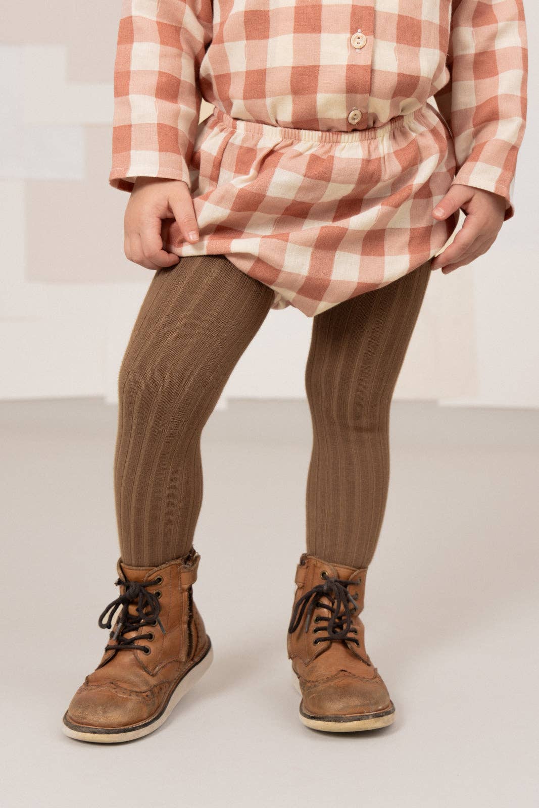 Person wearing a checkered dress, brown leggings, and brown boots on a white background