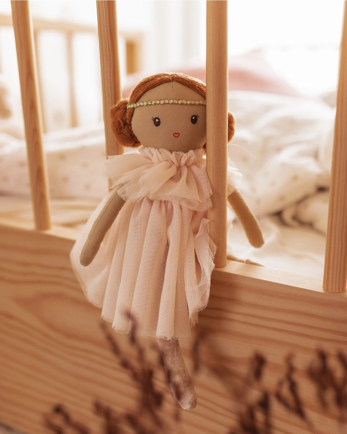 Small doll with a pink dress and brown hair in a crib
