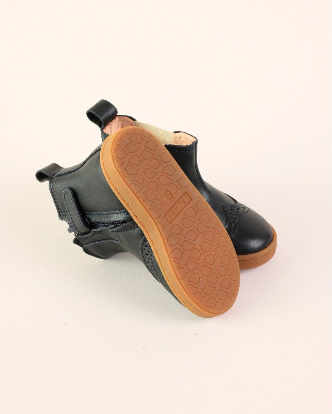 A pair of black leather ankle boots shown from the side, highlighting the tan rubber outsole and pull tab, set against a plain light beige background.