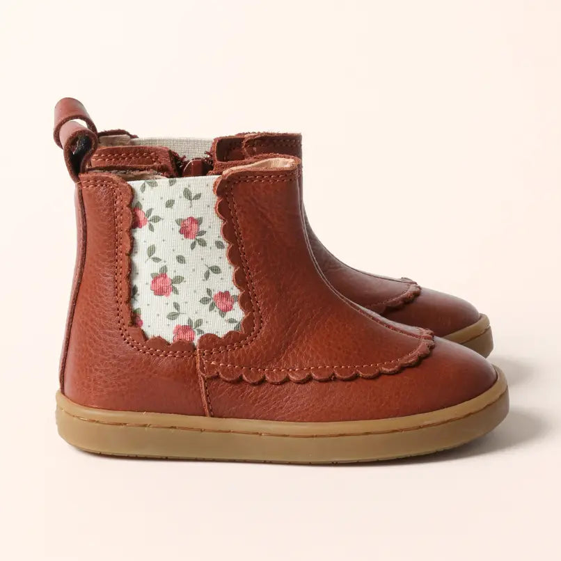 A pair of toddler ankle boots in brown leather with a floral patterned elastic side panel, set against a plain light beige background.