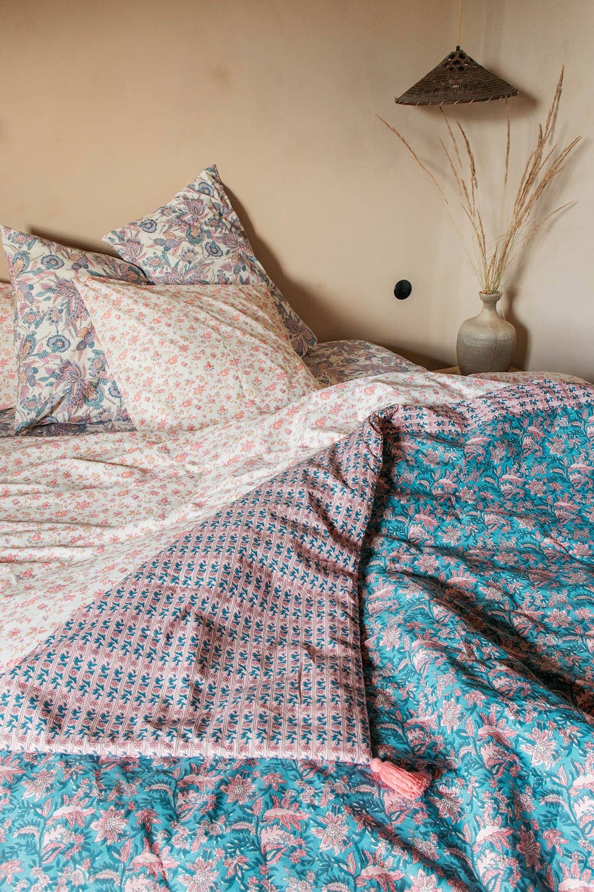 Floral patterned bedding on a bed with a lamp and decorative vase in the background.
