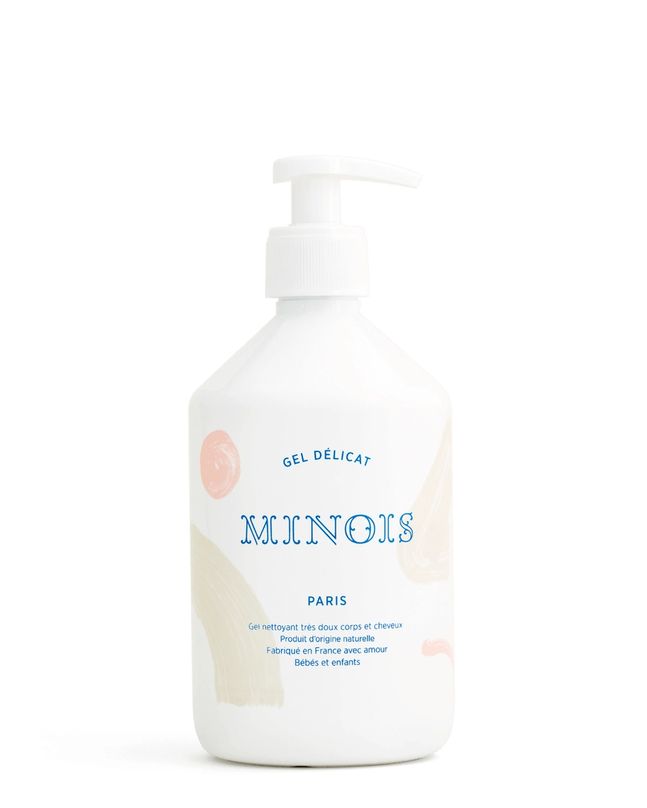 A white pump bottle of Minois Gel Delicat Paris baby lotion with a white dispenser, featuring blue text and soft pastel pink and beige abstract accents on the label, set against a plain white background.