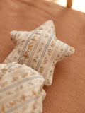 A star-shaped decorative pillow with a cream floral and striped pattern, resting on a textured terracotta-colored fabric surface.