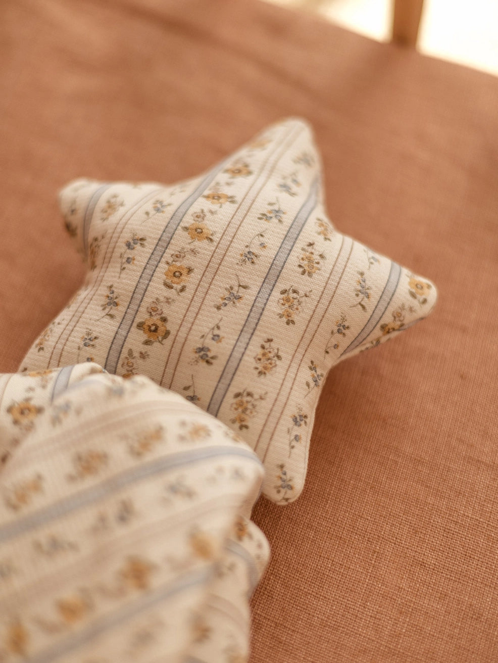 A star-shaped decorative pillow with a cream floral and striped pattern, resting on a textured terracotta-colored fabric surface.