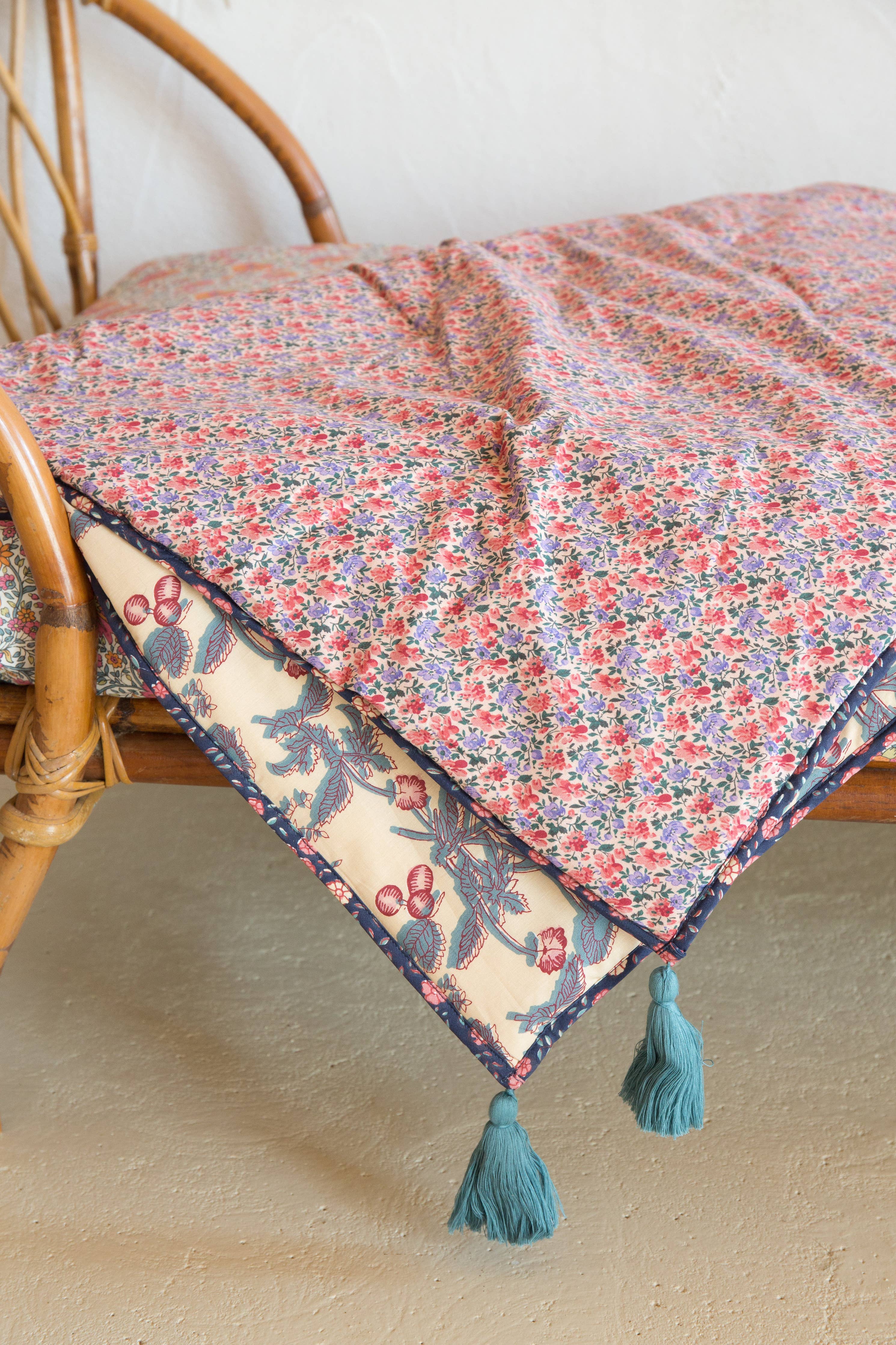 Floral patterned throw blanket with tassels draped over a wicker chair.