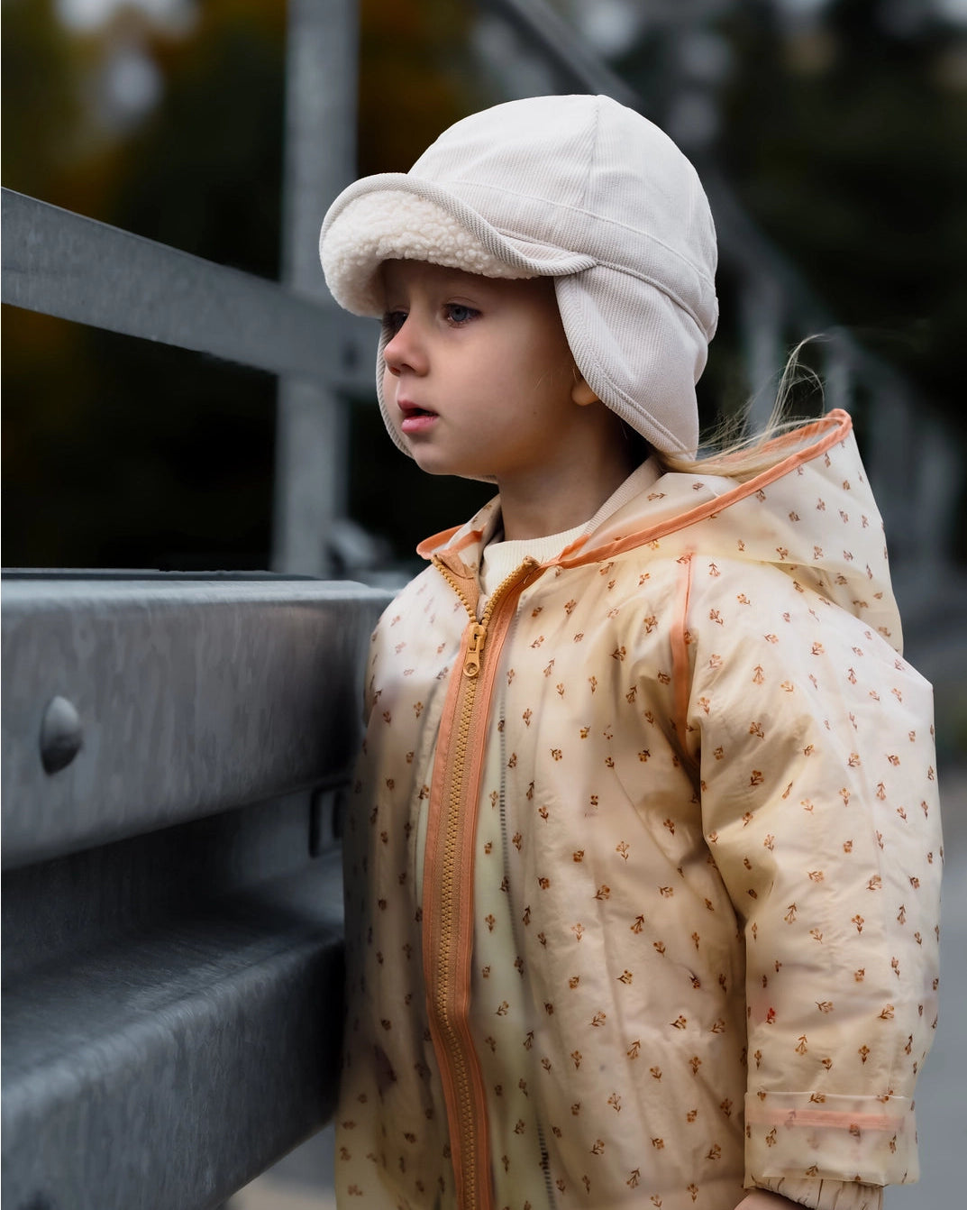 Child wearing a beige jacket and cap standing outdoors