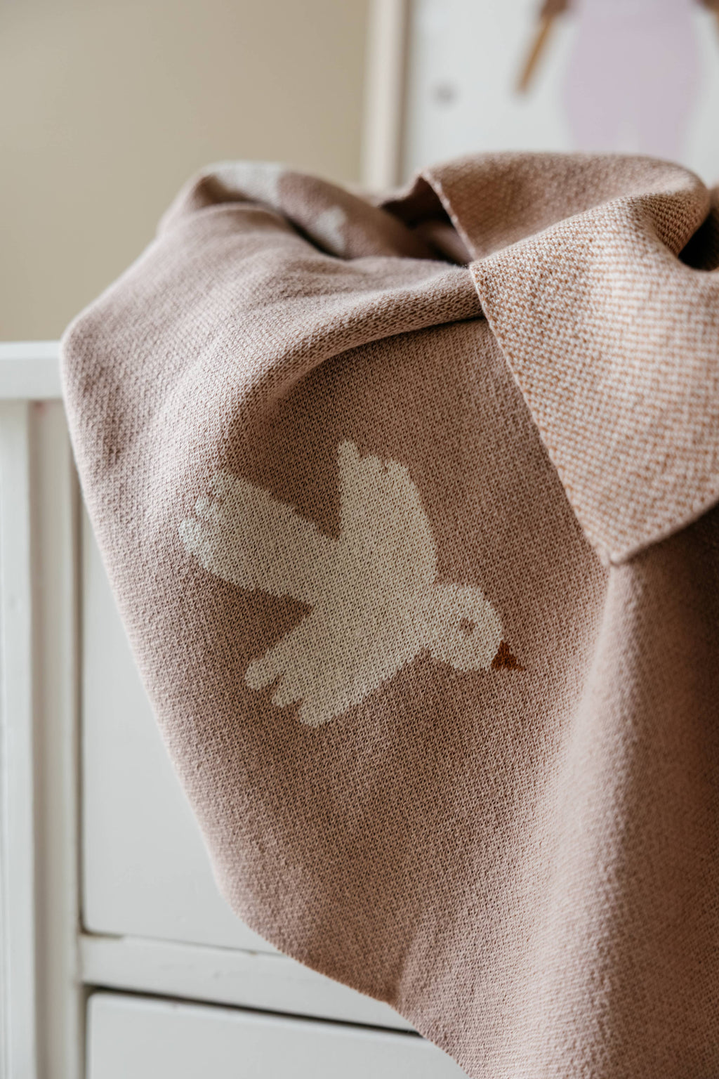 Brown blanket with a white bird design draped over a white surface.