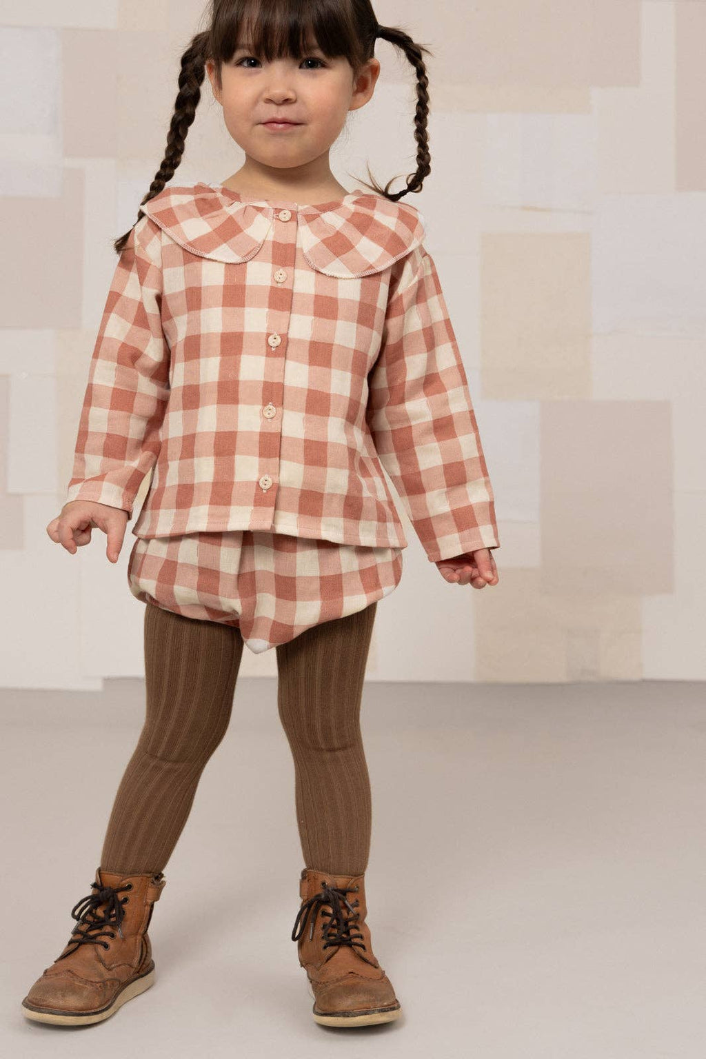 Child wearing a checkered shirt and brown pants with a neutral background