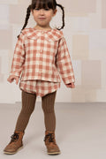 Child wearing a checkered shirt and brown pants with a neutral background