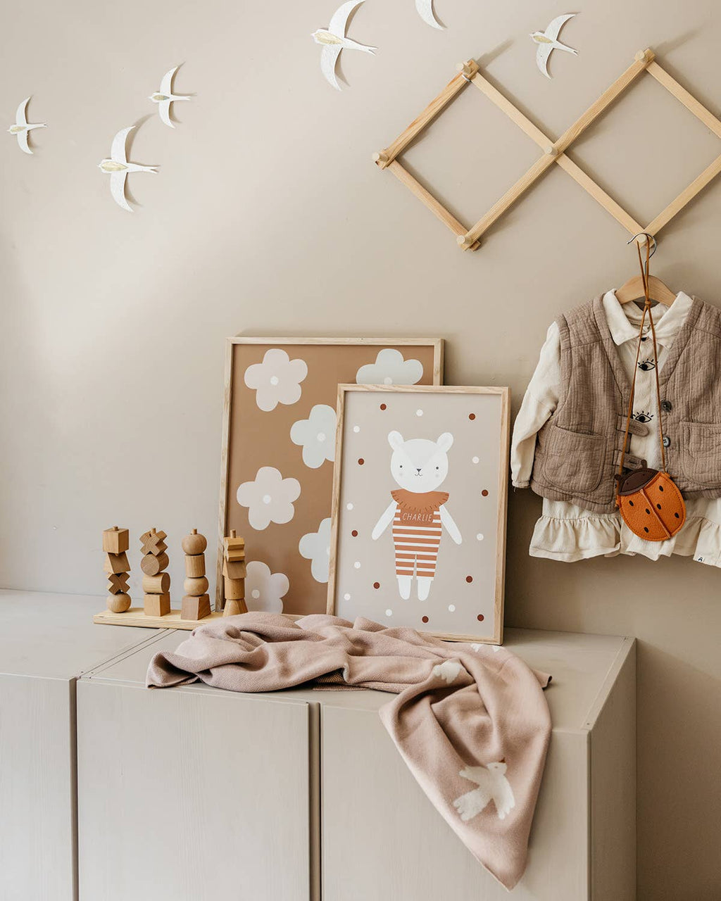Children's room with wooden toys, framed illustrations, and a baby outfit on a dresser.