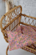 Floral-patterned cushion on a wicker chair against a textured wall.