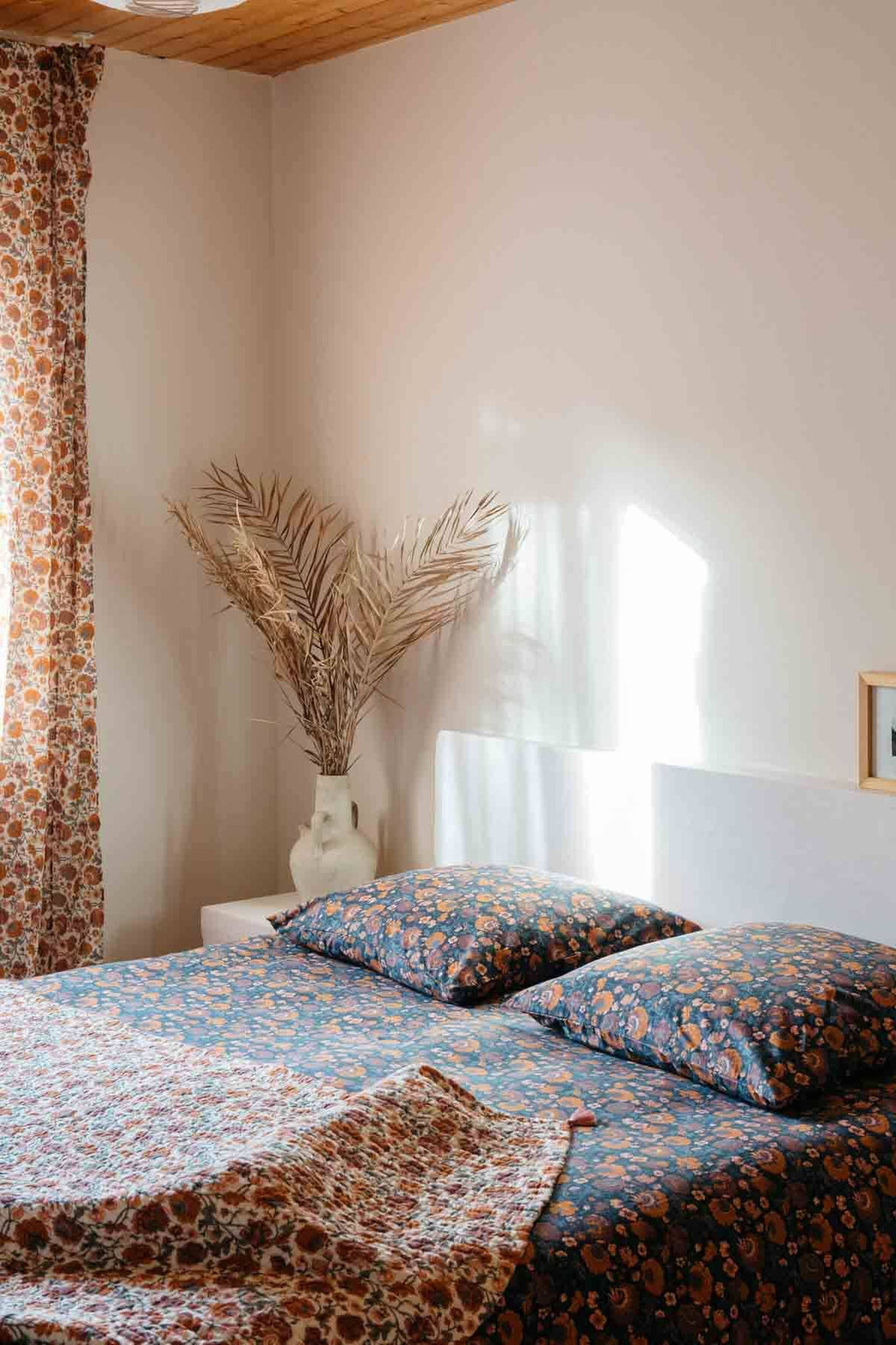 Bedroom with floral-patterned bedding and curtains, natural light coming through a window.