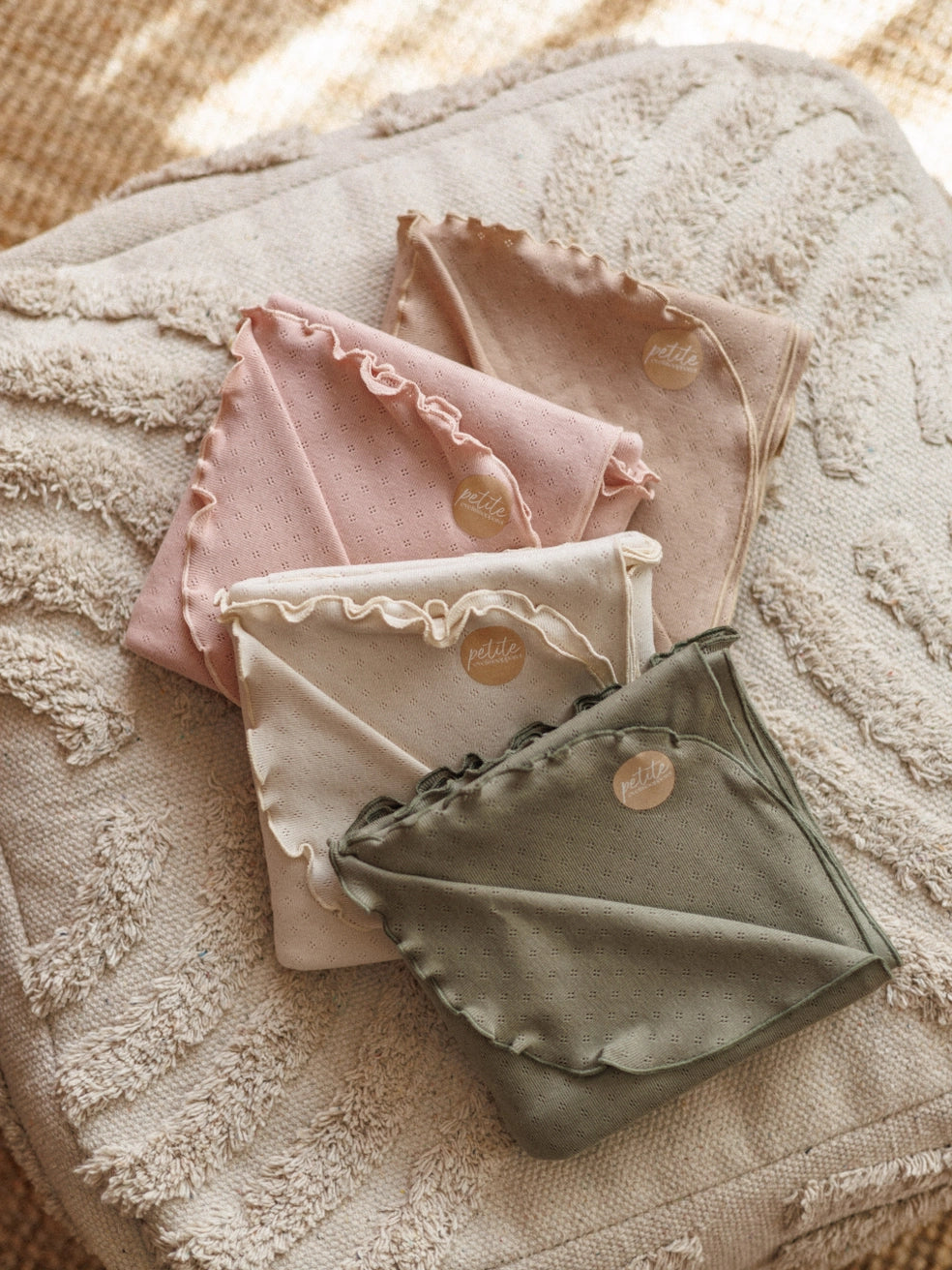 Folded baby blankets in pink, beige, and green on a textured surface