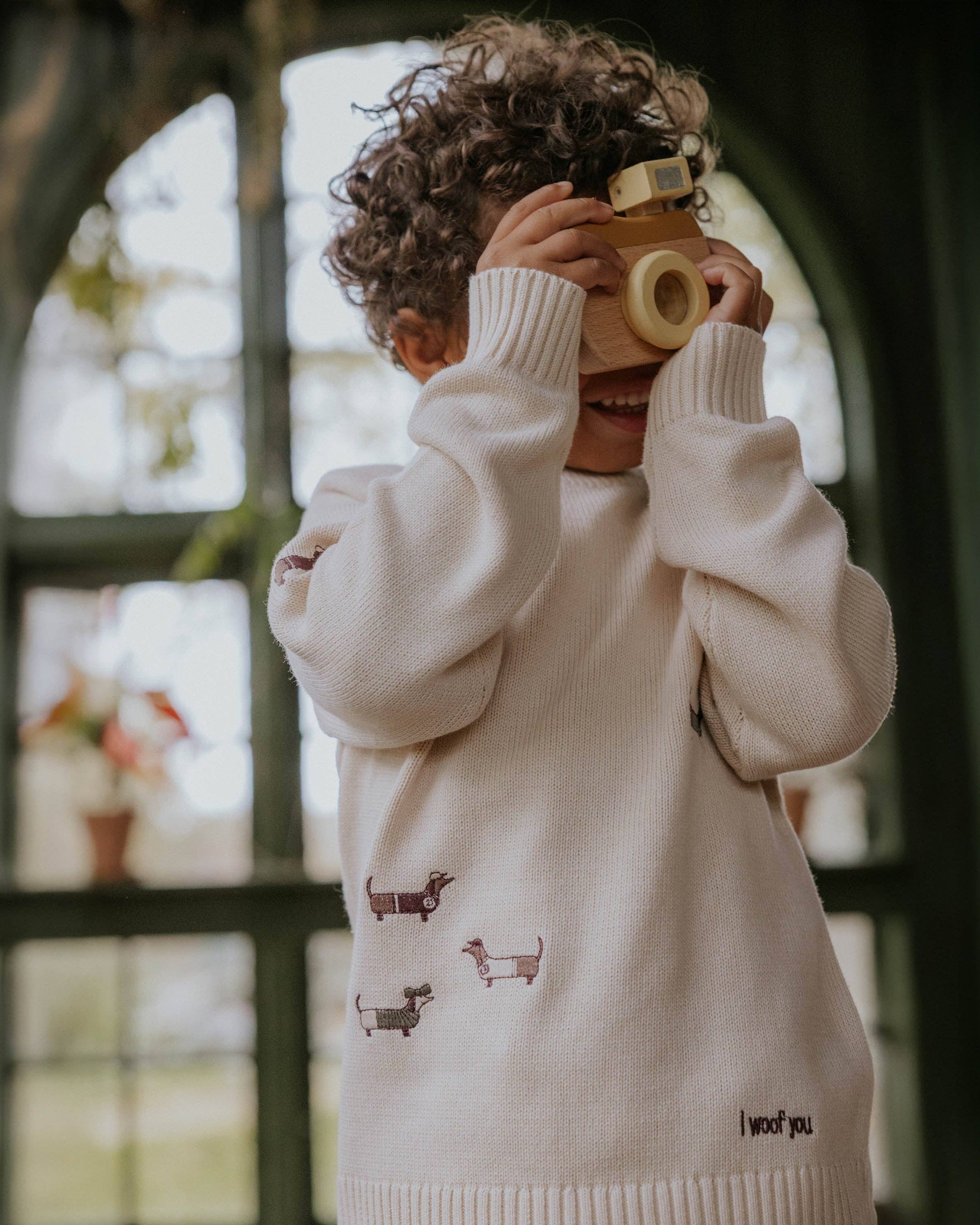 Child wearing a cream sweater with small prints, holding a vintage camera.
