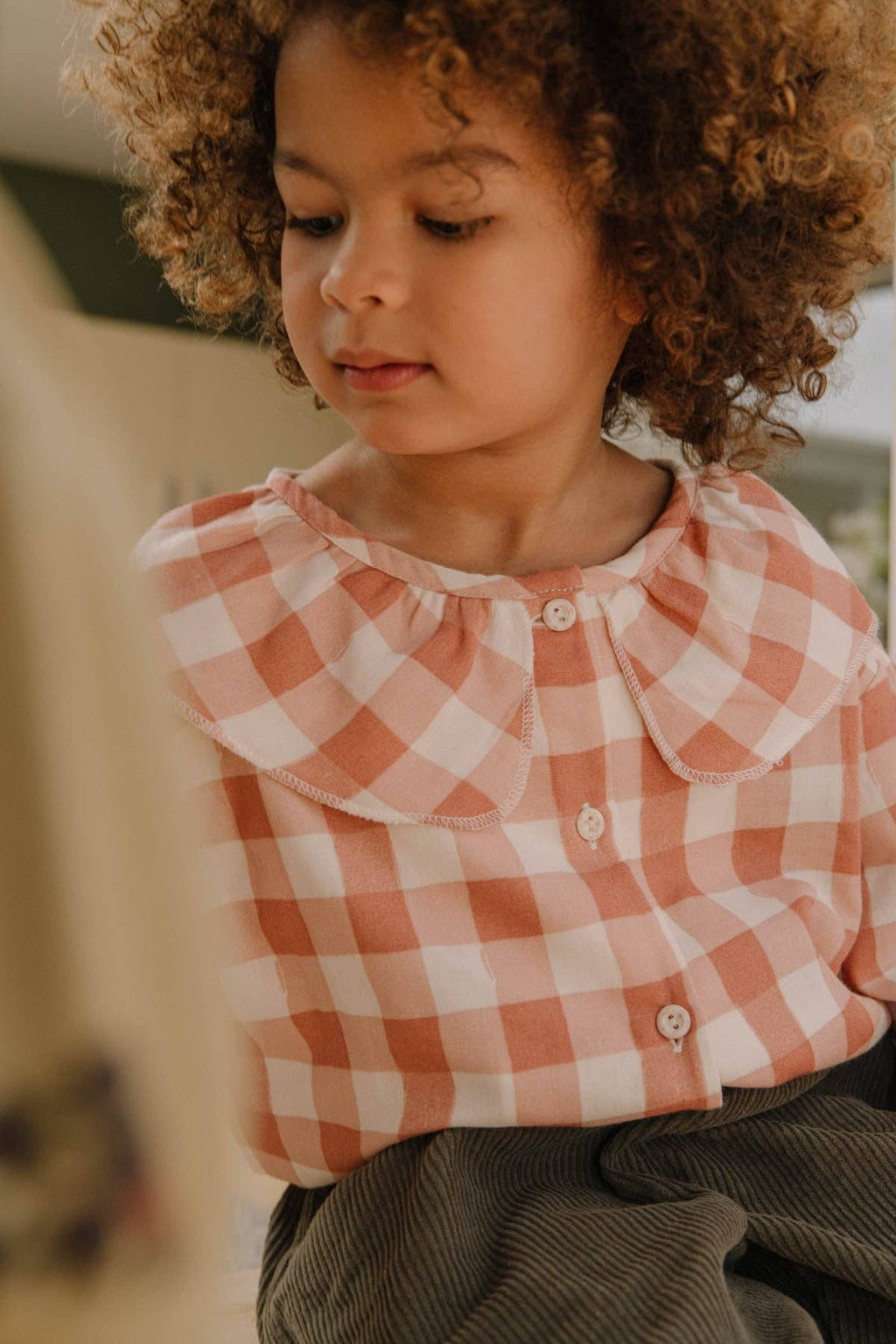 Child wearing a pink and white checkered shirt with a blurred background