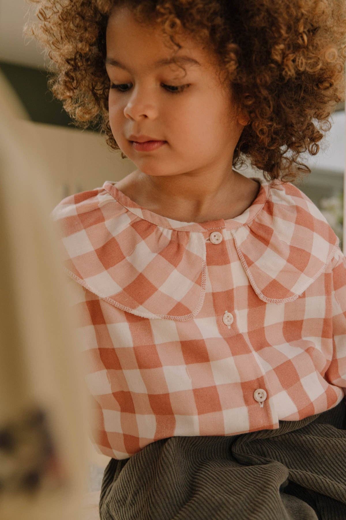 Child wearing a pink and white checkered shirt with a blurred background