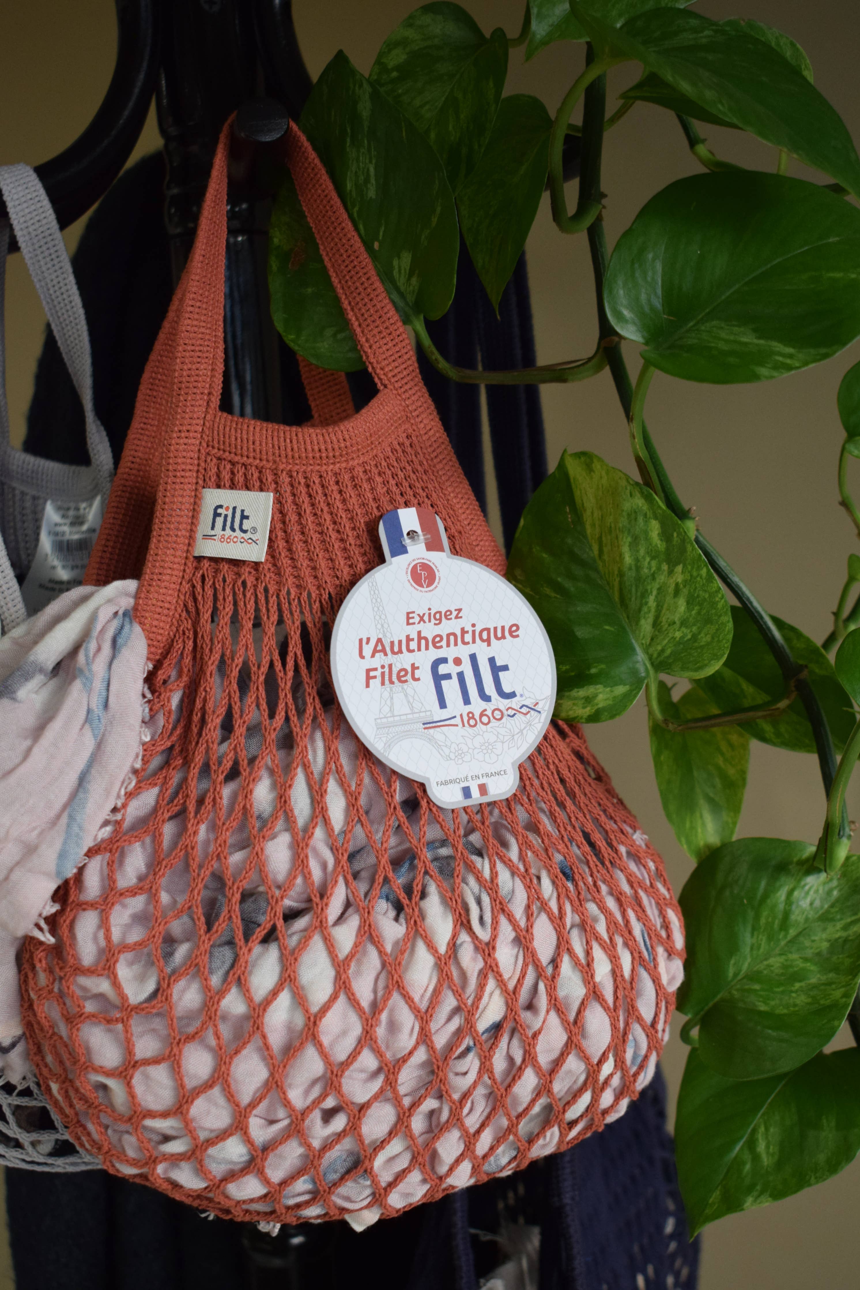 Orange mesh bag with Filt label hanging on a plant