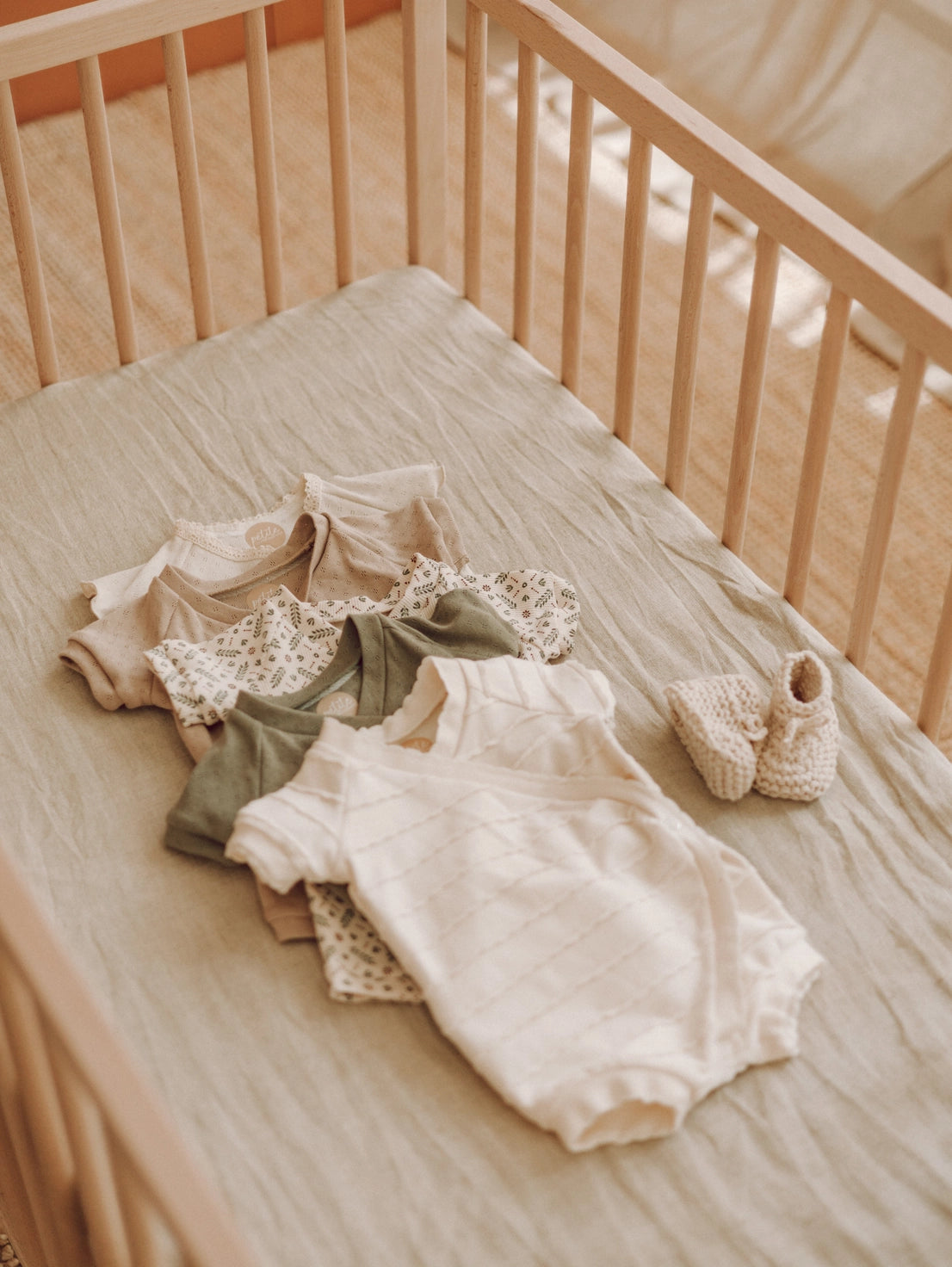 Baby clothes and shoes on a crib with a neutral color palette