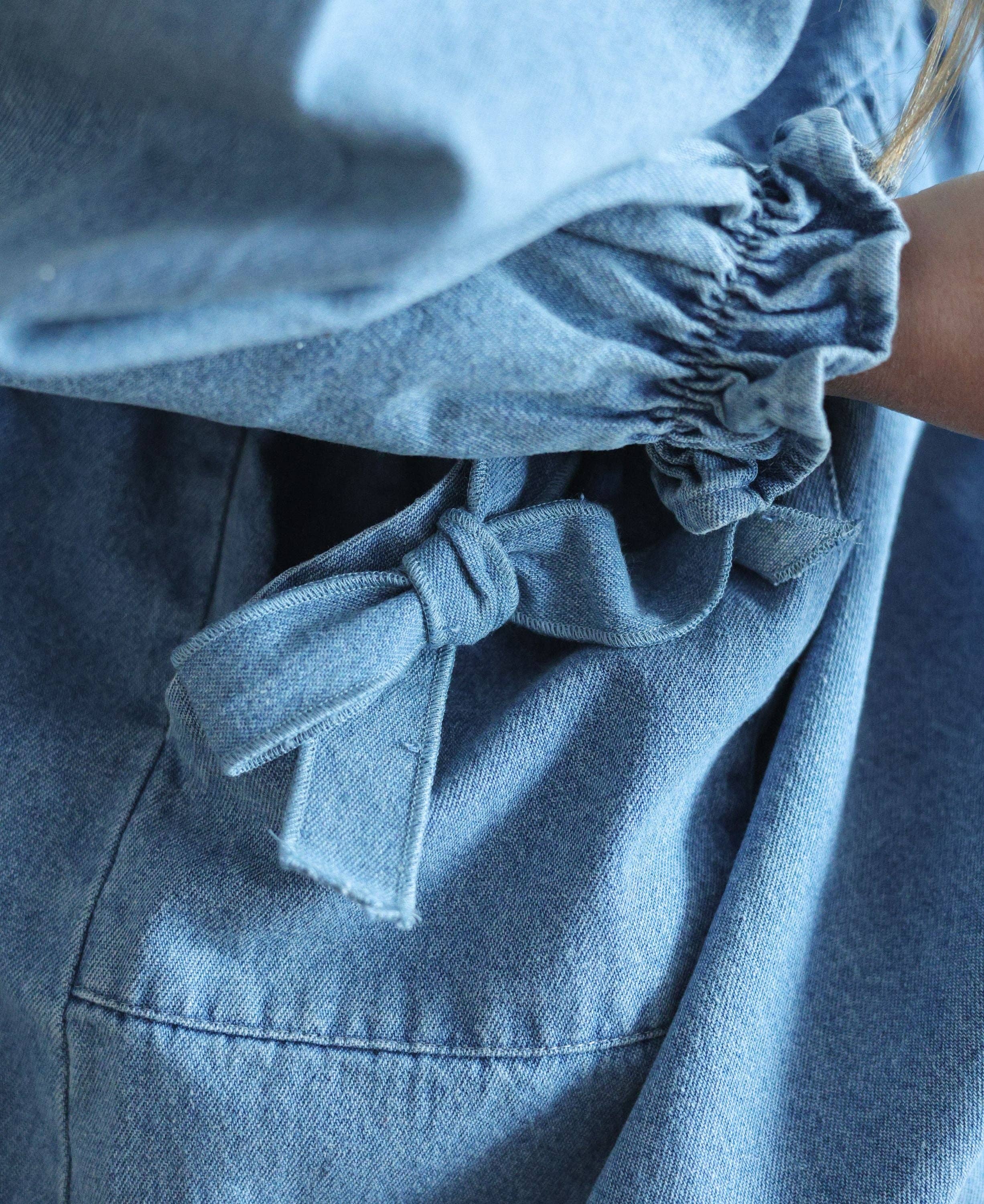Close-up of a blue denim dress with a bow detail.