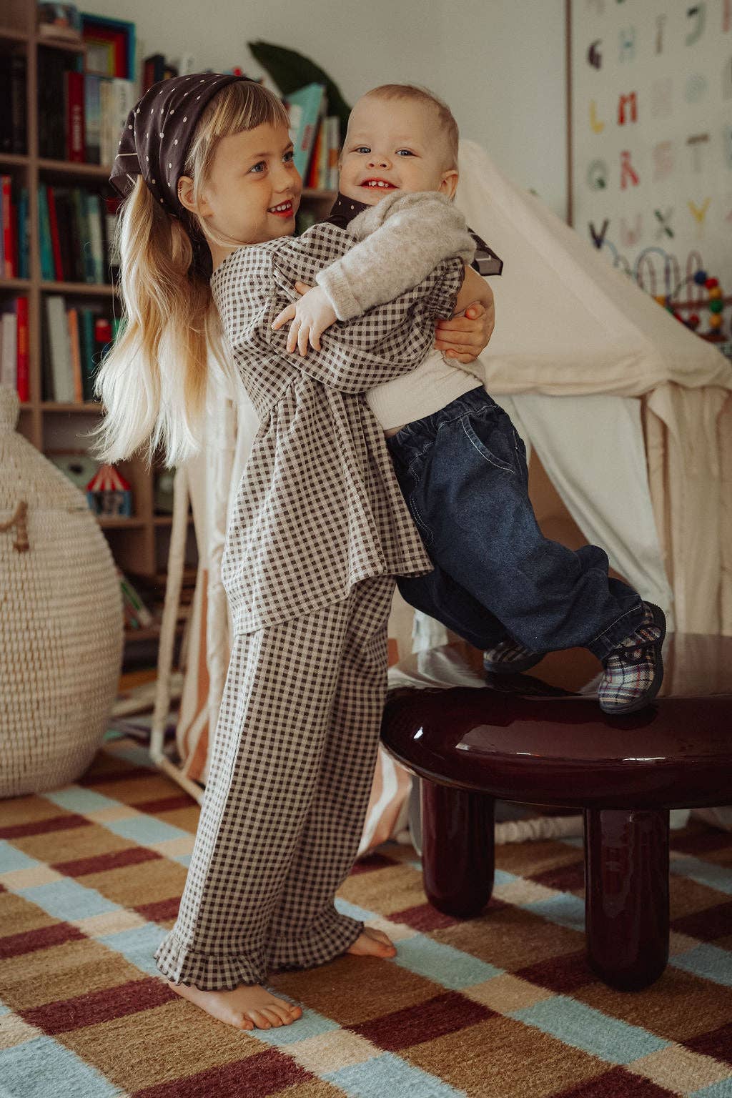 Two children playing together in a room with books and a small tent.