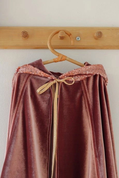 Brown velvet skirt with lace trim hanging on a wooden hanger against a white wall.