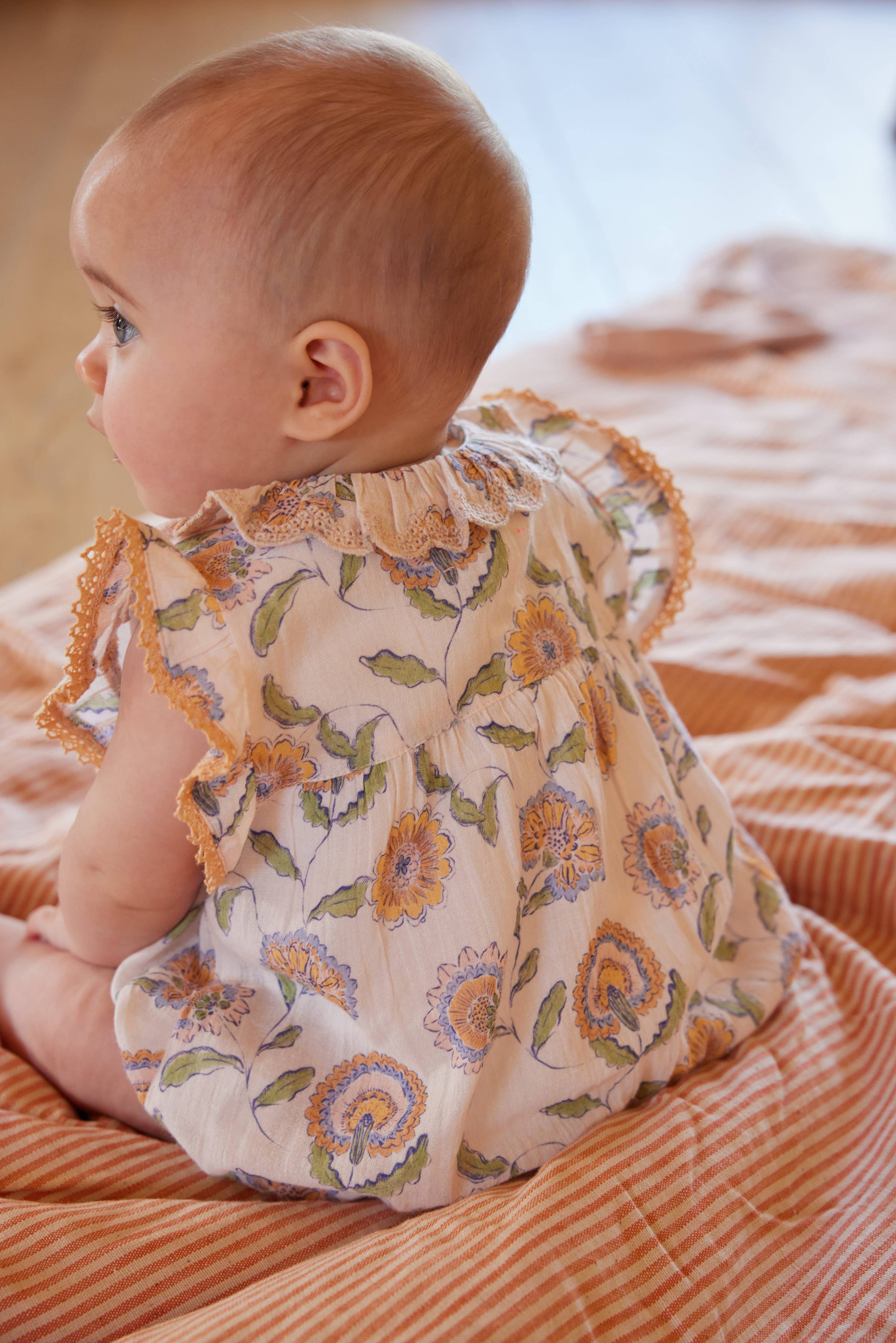 Baby wearing a floral dress sitting on an orange blanket