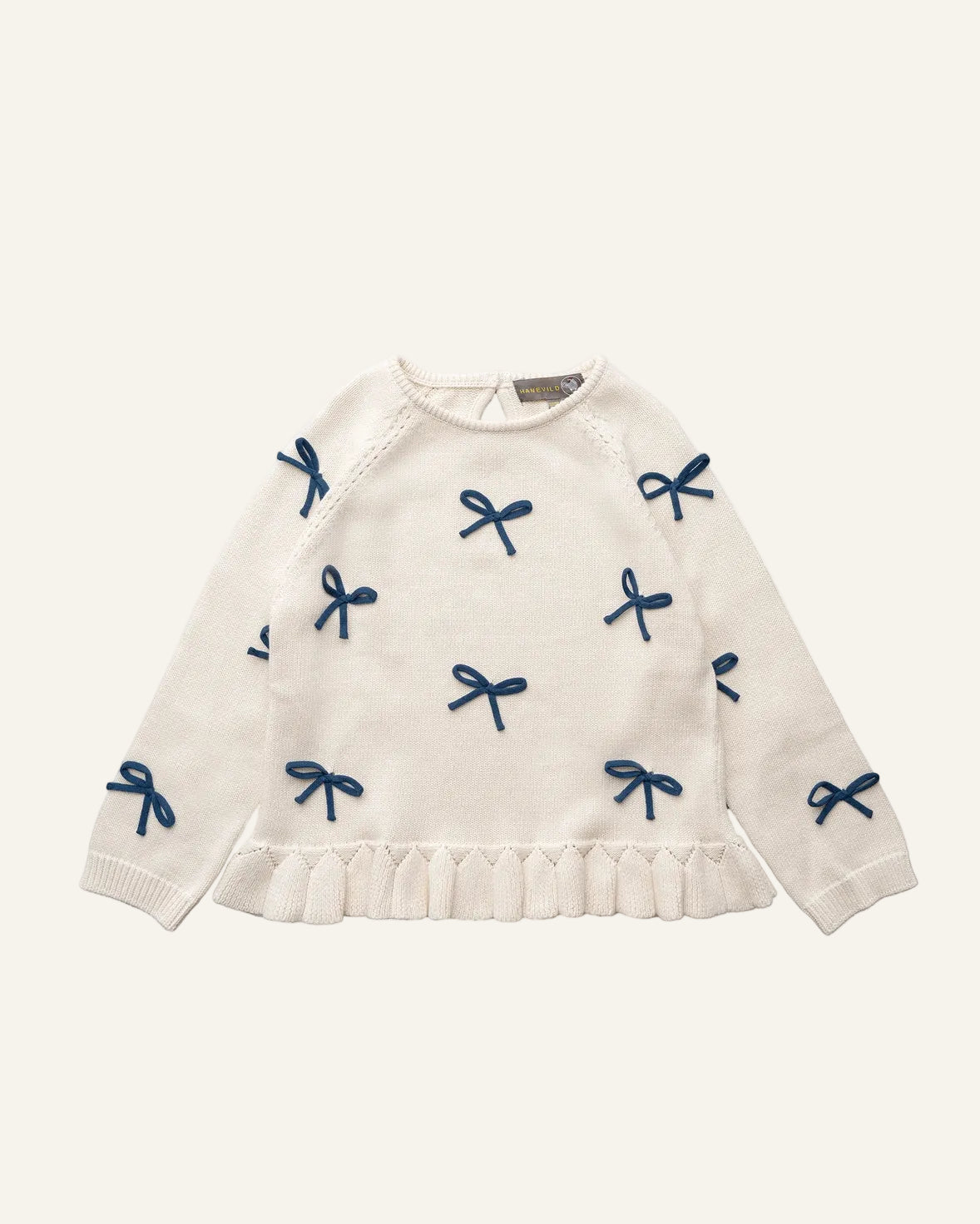 An off-white knit sweater for toddlers, featuring an all-over navy blue bow pattern and a ruffled hem, displayed on a clean white background.