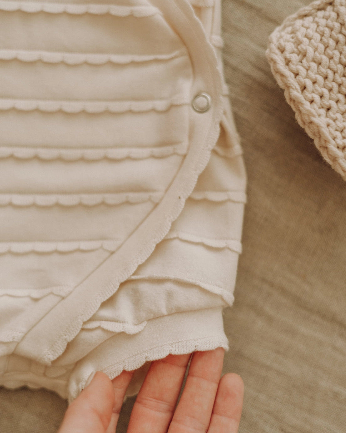Close-up of a beige ruffled fabric with a hand holding it, on a neutral background.