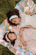 Two young girls lying on a colorful quilt in a grassy area