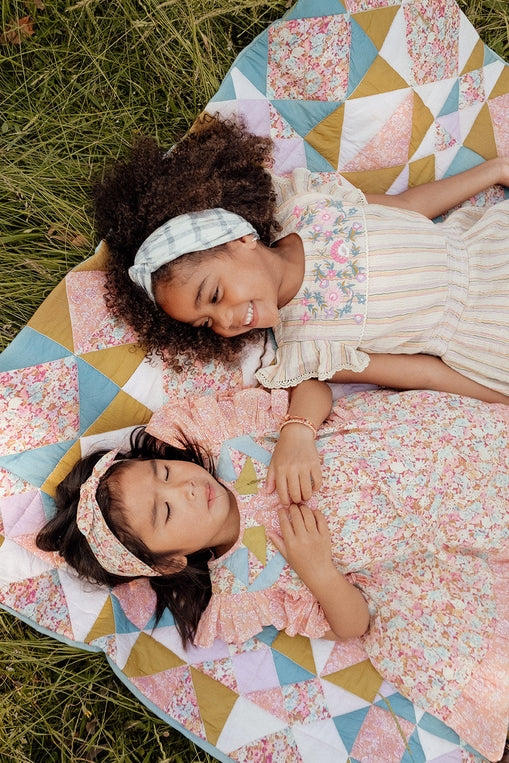 Two young girls lying on a colorful quilt in a grassy area