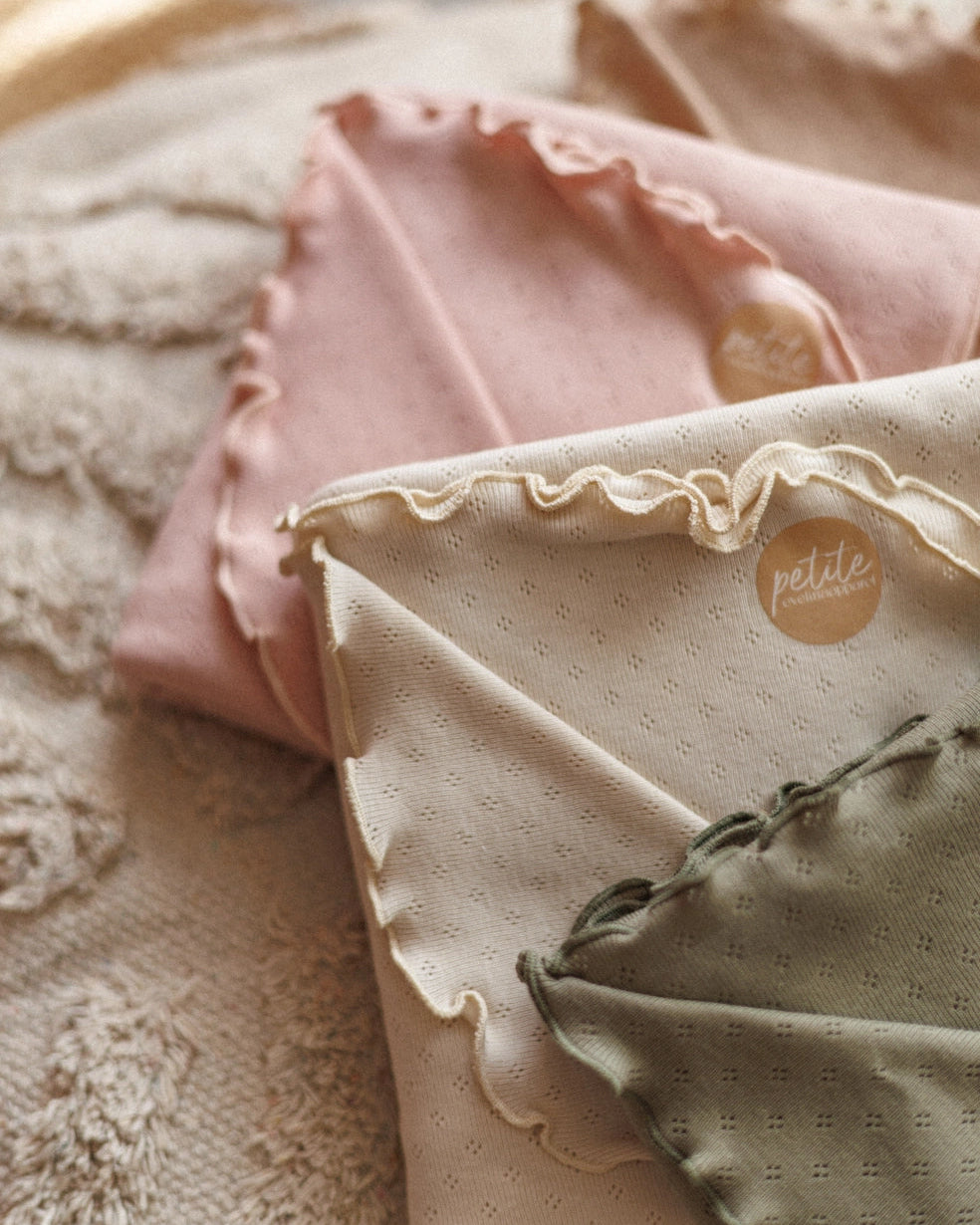 Folded baby clothes with 'petite' brand logo on a textured surface
