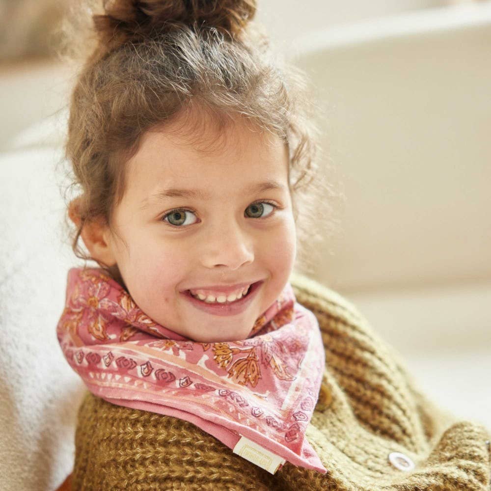 Child wearing a pink patterned scarf and brown sweater, smiling.
