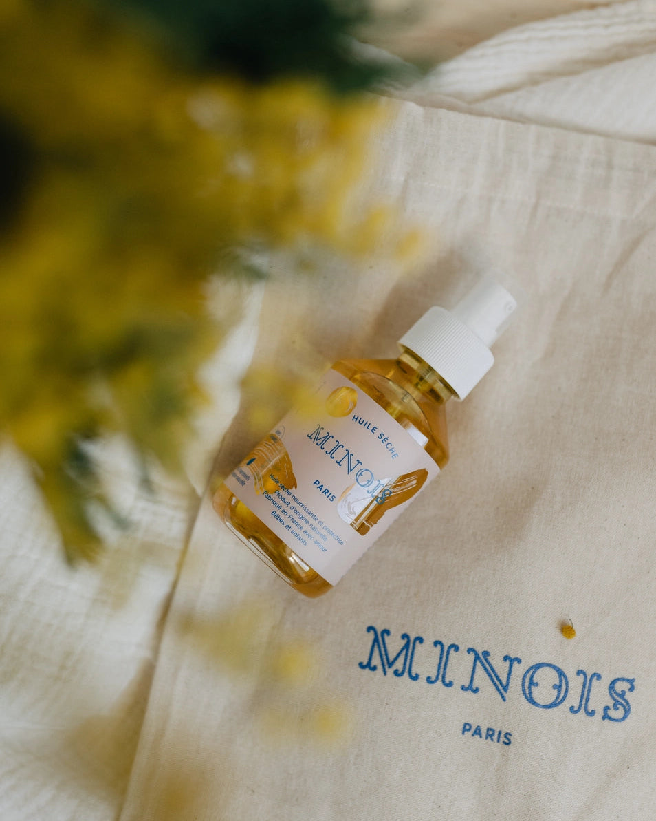 Bottle of Minois Paris on a beige fabric background with flowers in the corner