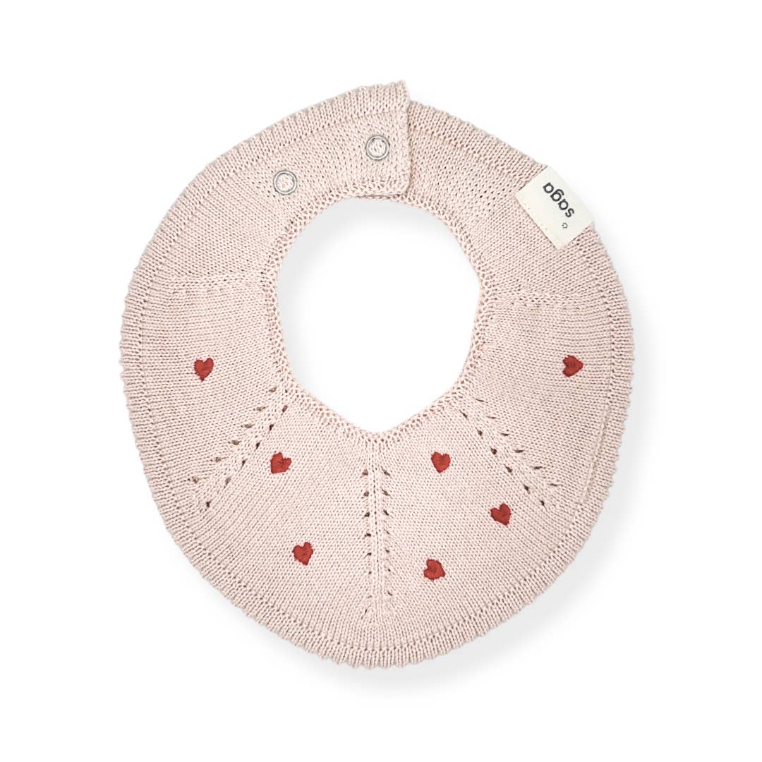 A light pink knitted baby bib with small red heart patterns and silver snap closures, shown on a clean white background.