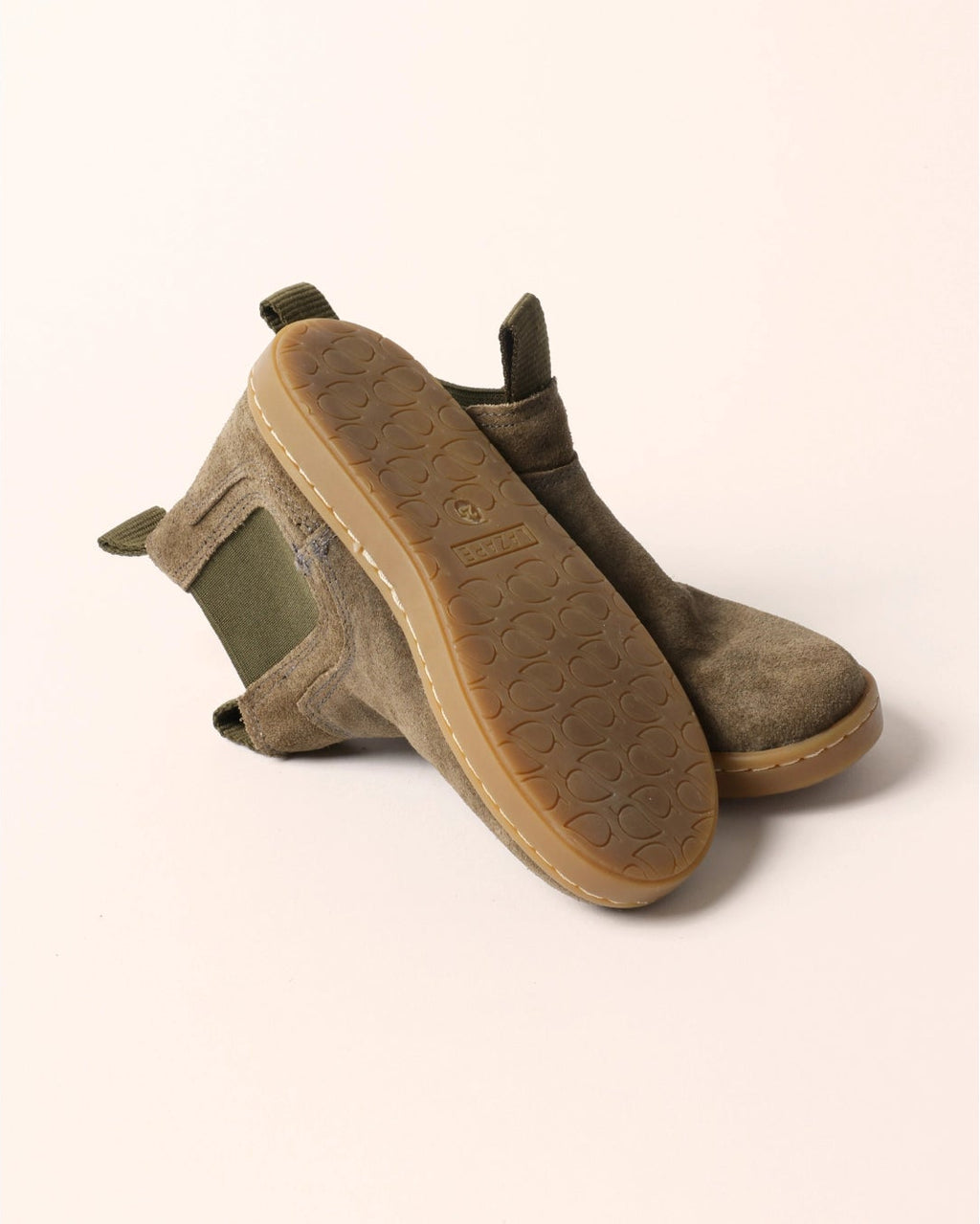 A pair of low-top ankle boots in a muted olive-brown suede and leather mix, shown from a three-quarters angle on a solid pale pink background.