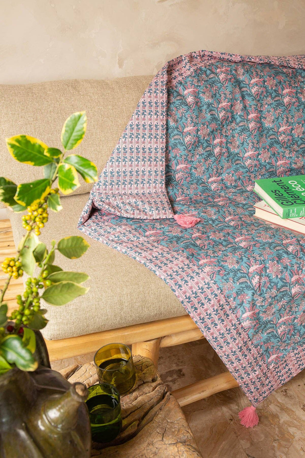Floral patterned throw blanket draped over a sofa with a plant and books in the foreground.